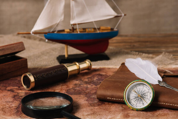 ship, telescope, magnifying glass, leather copy book and nib on old world map and hessian