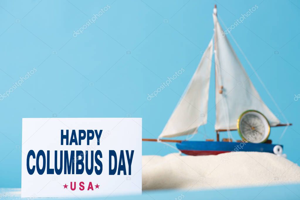 carta con iscrizione felice Columbus Day vicino nave in miniatura in sabbia bianca isolata su blu
