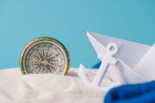 bílý písek s papírovým člunem, kotevním a kompasem izolovaným na modré