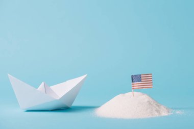 paper boat near American national flag in white sand on blue background clipart