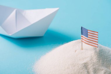 mavi arka plan üzerinde Amerikan ulusal bayrağı ile kum yakınında beyaz kağıt tekne
