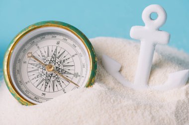 plastic anchor and compass in white sand isolated on blue clipart