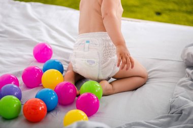 Renkli toplar arasında yatakta oturan bebek bezi sevimli bebek Kırpılmış görünümü