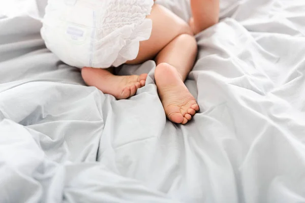 Vista parcial del pequeño pie de bebé y el pañal en la cama blanca —  Fotos de Stock