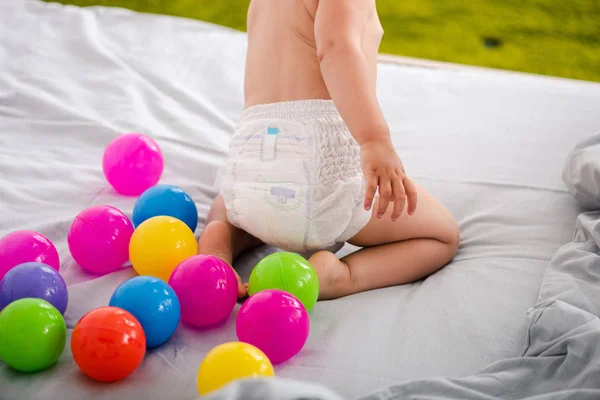 Vágott kilátás aranyos baba pelenka ül az ágyban között színes golyók — Stock Fotó
