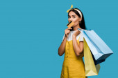 mladá žena držící kreditní kartu a nákupní tašky izolované na modré 