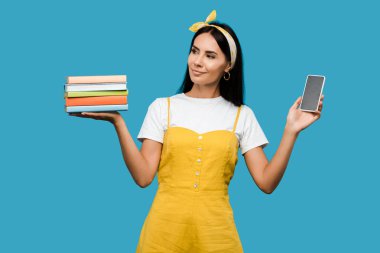 mavi izole boş ekran ile kitap ve akıllı telefon tutan genç kadın 