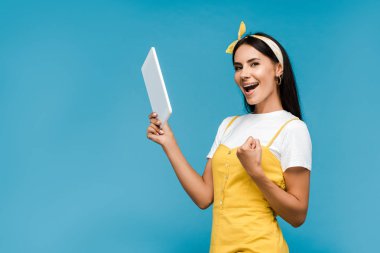 mutlu kız dijital tablet tutan ve mavi izole sıkıştırılmış yumruk ile ayakta 
