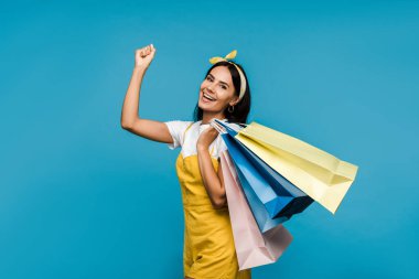 renkli alışveriş çantaları tutan mutlu genç kadın ve mavi izole gesturing 
