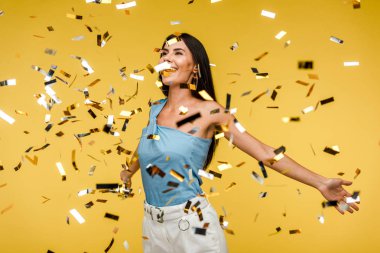 selective focus of cheerful woman near sparkling confetti on orange  clipart