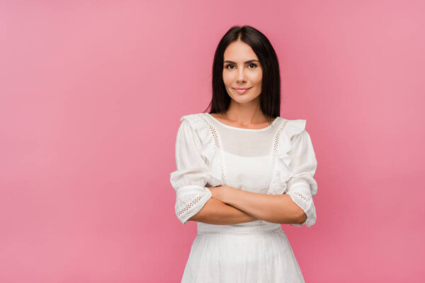 attractive woman in dress standing with crossed arms isolated on pink 