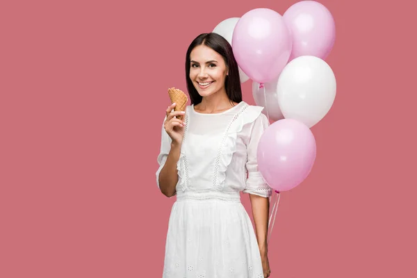 ピンクに隔離された風船とアイスクリームコーンを保持するドレスの笑顔の女の子 — ストック写真