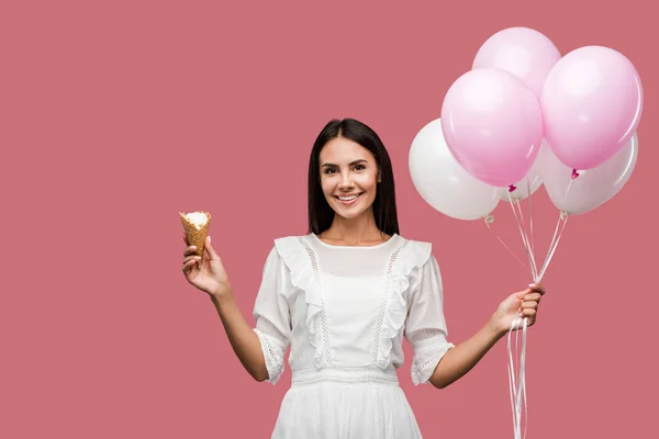 ピンクに隔離された風船とアイスクリームコーンを保持するドレスの陽気な女の子 — ストック写真