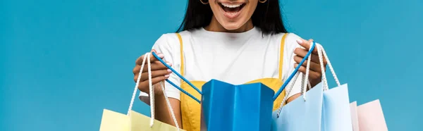 青で隔離されたカラフルなショッピングバッグを持つ幸せな若い女性のパノラマショット — ストック写真