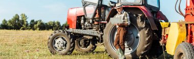 panoramic shot of farmer in straw hat using laptop near tractor  clipart