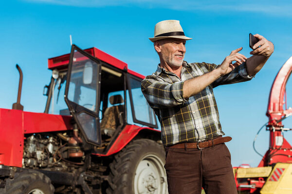selective focus of happy self-employed farmer taking selfie near tractor 
