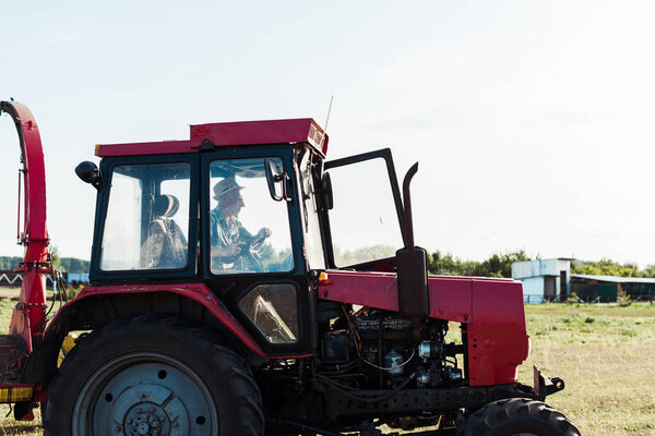 bearded senior farmer in straw hat driving tractor 