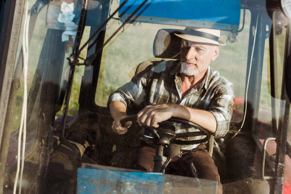 selective focus of cheerful self-employed farmer smiling while driving tractor 