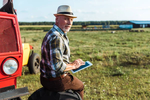 赤いトラクターの近くにデジタルタブレットを使用してわら帽子で幸せな農家 — ストック写真