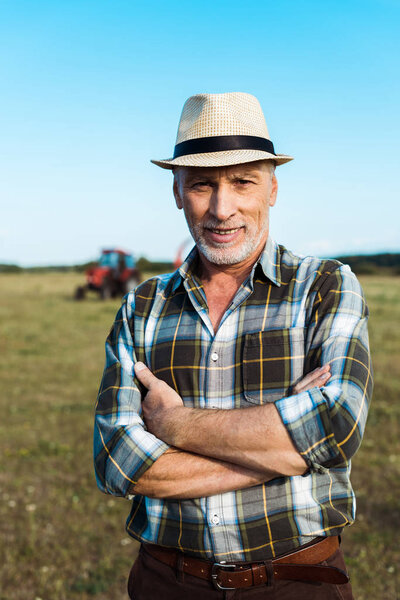 cheerful senior farmer standing with crossed arms in field 