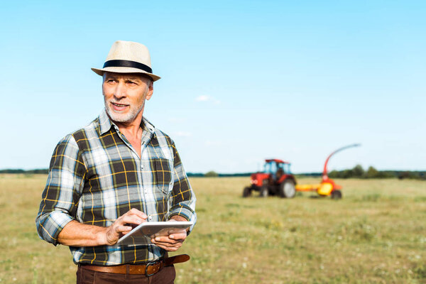 cheerful self-employed farmer in straw hat using digital tablet in field 