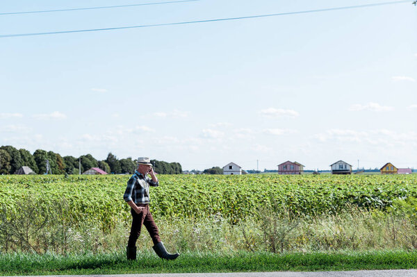 bearded self-employed farmer talking on smartphone while walking in field