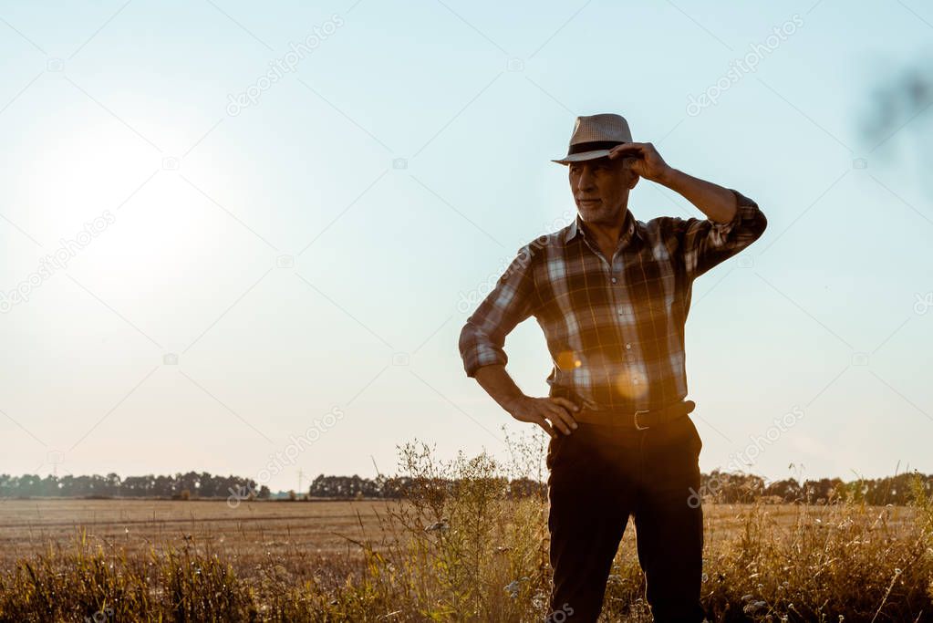 senior man touching straw hat in wheat field 