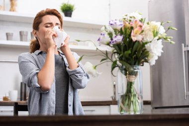 selective focus of woman with pollen allergy sneezing in tissue near flowers  clipart