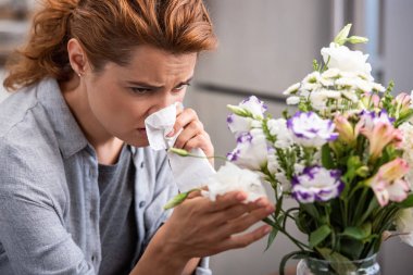 selective focus of woman with pollen allergy holding tissue and touching flowers  clipart