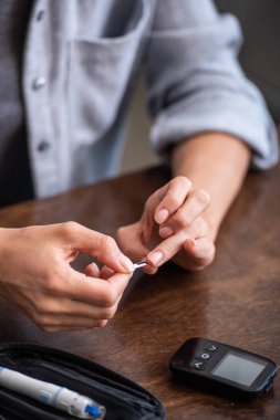 evde glikoz monitörü yakınında kan testi yapan kadının kırpılmış görünümü 