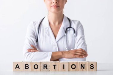 cropped view of doctor with crossed arms near cubes with abortion letters  clipart