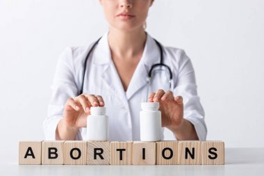 cropped view of doctor touching bottles on cubes with abortion letters  clipart