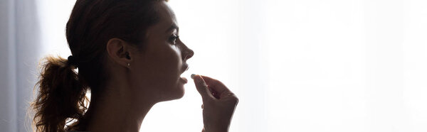 panoramic shot of attractive woman taking pill at home 