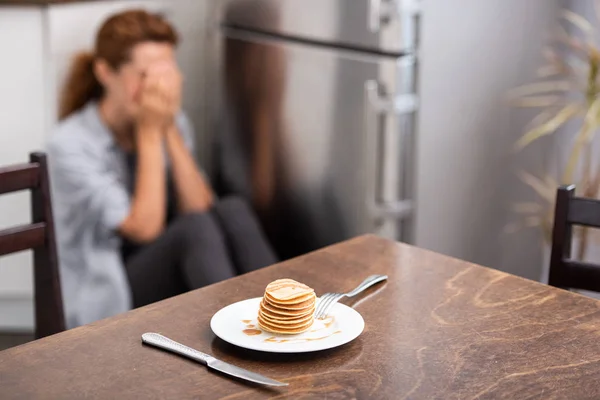 床に座って顔を覆う女性の近くのテーブルの上においしいパンケーキの選択的な焦点 — ストック写真