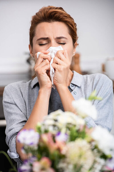 selective focus of woman with pollen allergy sneezing in tissue near flowers 