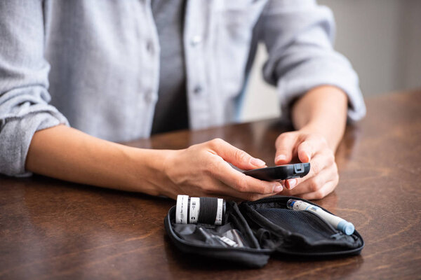 cropped view of woman holding glucose monitor near first aid kit 