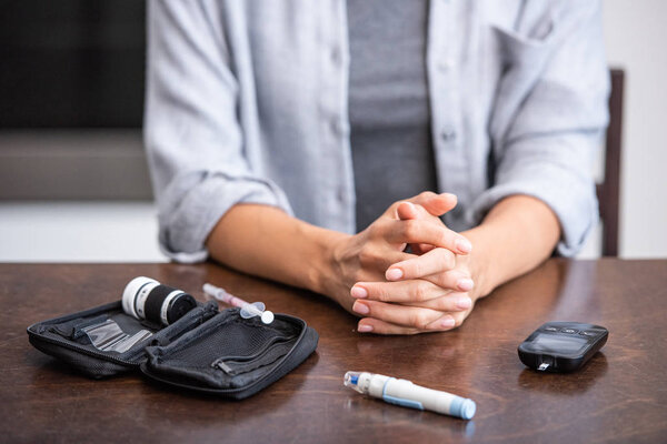 cropped view of woman sitting with clenched hands near first aid kit and blood lancet