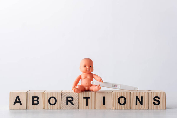 baby doll near pregnancy test and wooden cubes with lettering on white 
