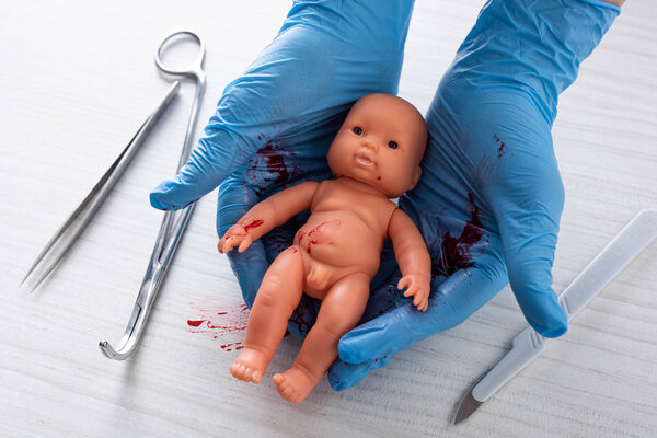 cropped view of doctor in blue latex gloves holding baby doll near medical instruments 
