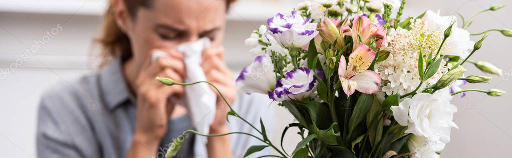 panoramic shot of bouquet of flowers near woman with pollen allergy sneezing in tissue 