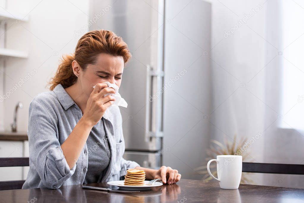 sick woman sneezing in tissue near sweet pancakes at home 