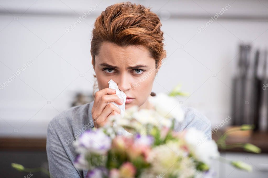 selective focus of sick woman with pollen allergy holding tissue near flowers 