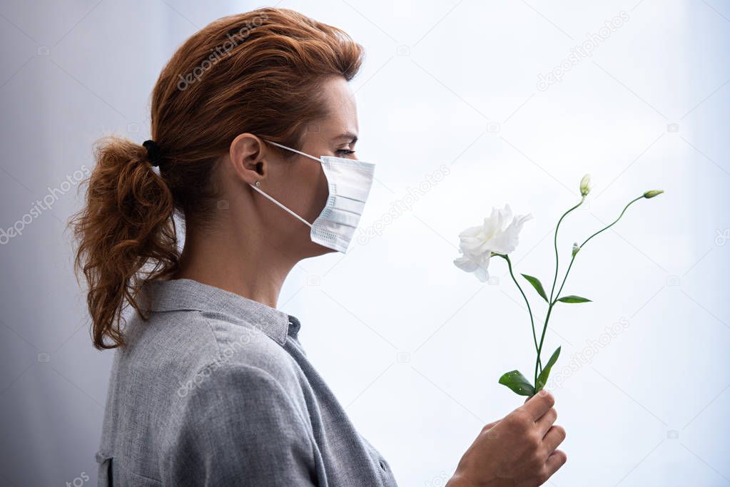 side view of woman in medical mask looking at flowers 