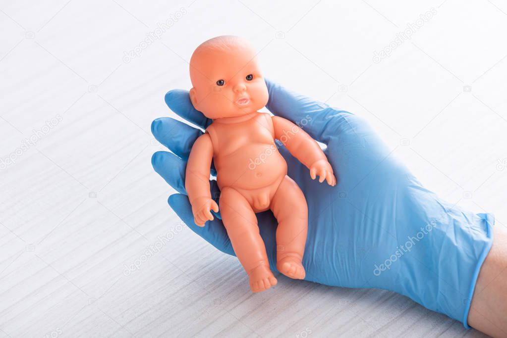 cropped view of doctor holding baby doll