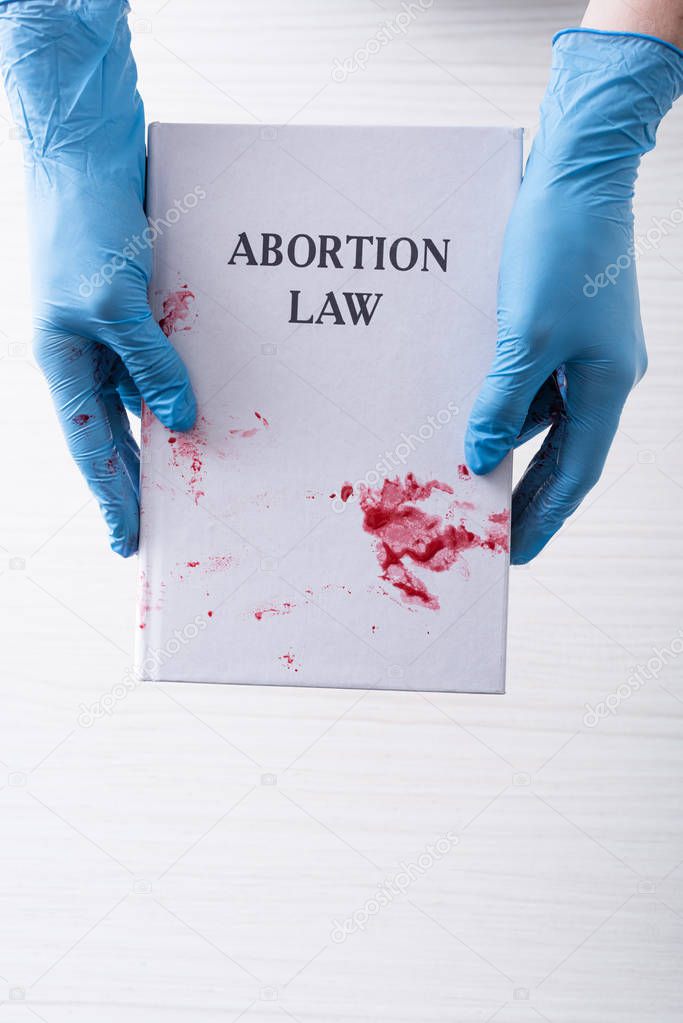 top view of doctor in latex gloves holding book with abortion law letters 