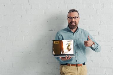 yakışıklı ve gülümseyen işadamı başparmak gösteren ve bilet online web sitesi ile dizüstü tutma