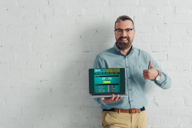 yakışıklı ve gülümseyen işadamı başparmak gösteren ve spor bahis web sitesi ile dizüstü tutma 