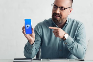 KYIV, UKRAINE - AUGUST 27, 2019: handsome businessman in shirt pointing with finger at smartphone with shazam logo