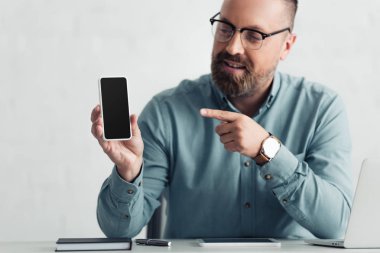 handsome businessman in shirt pointing with finger at smartphone with copy space
