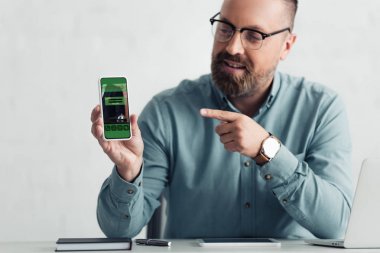 handsome businessman in shirt pointing with finger at smartphone with booking website 